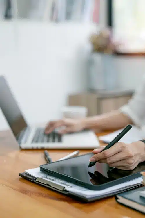 Escritora trabajando en su proceso creativo utilizando herramientas digitales, tablet y ordenador en un ambiente luminoso.